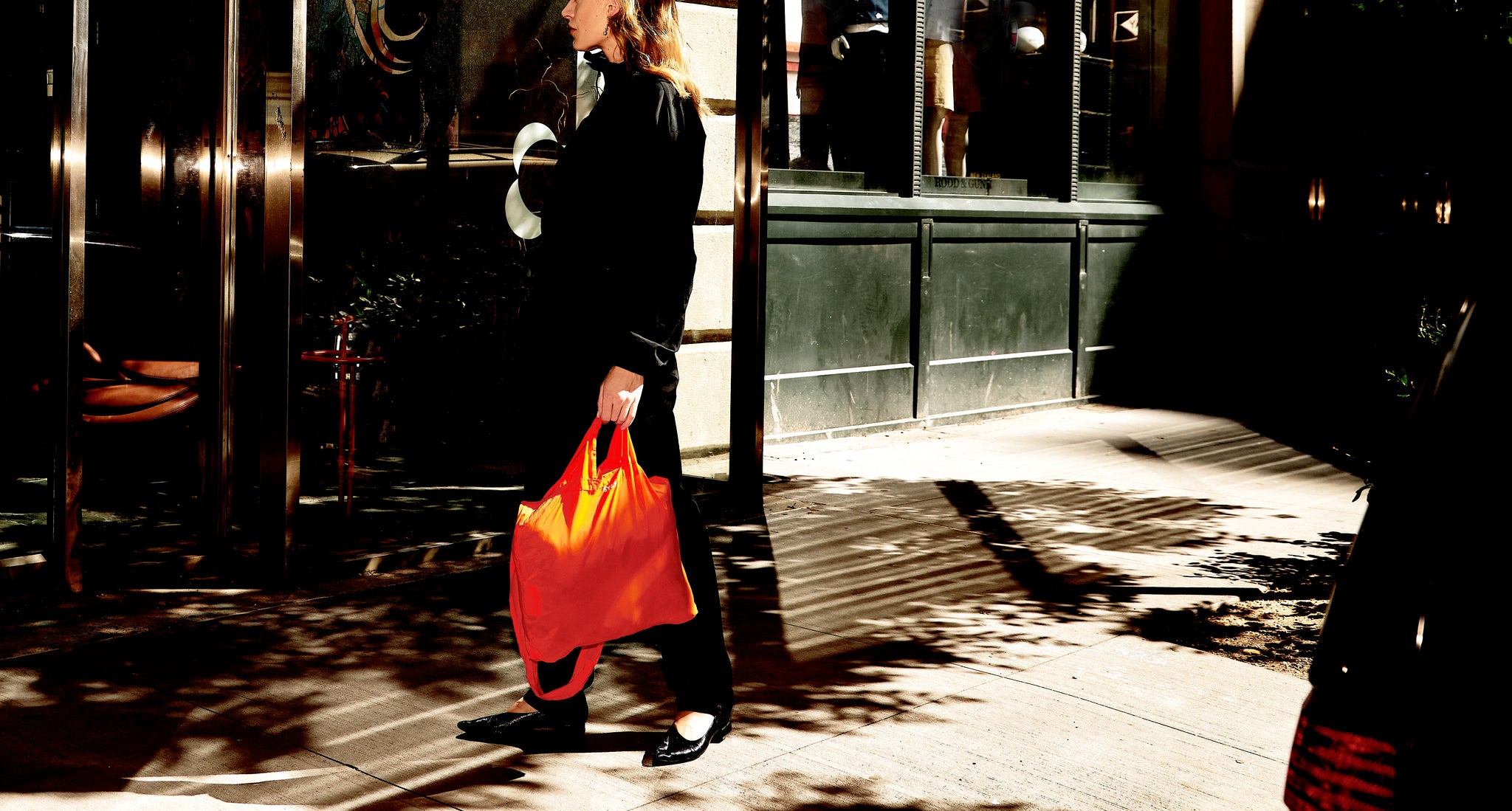 A women holding a Torri Orange TETRA Tote Bag near a store. 