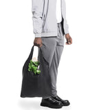 A person carrying a reusable black SYZY 
bag filled with groceries, including fresh green lettuce, highlighting its eco-friendly and durable design."