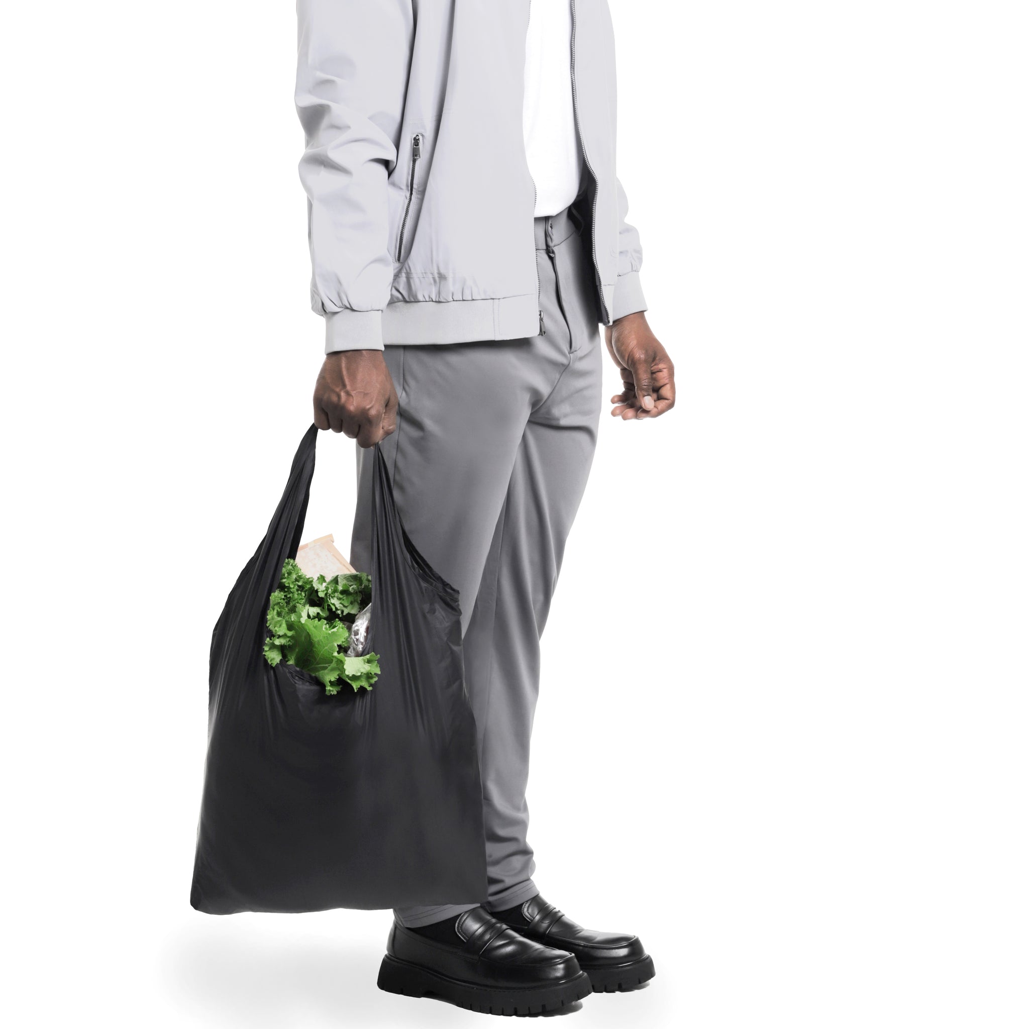 A person carrying a reusable black SYZY 
bag filled with groceries, including fresh green lettuce, highlighting its eco-friendly and durable design."